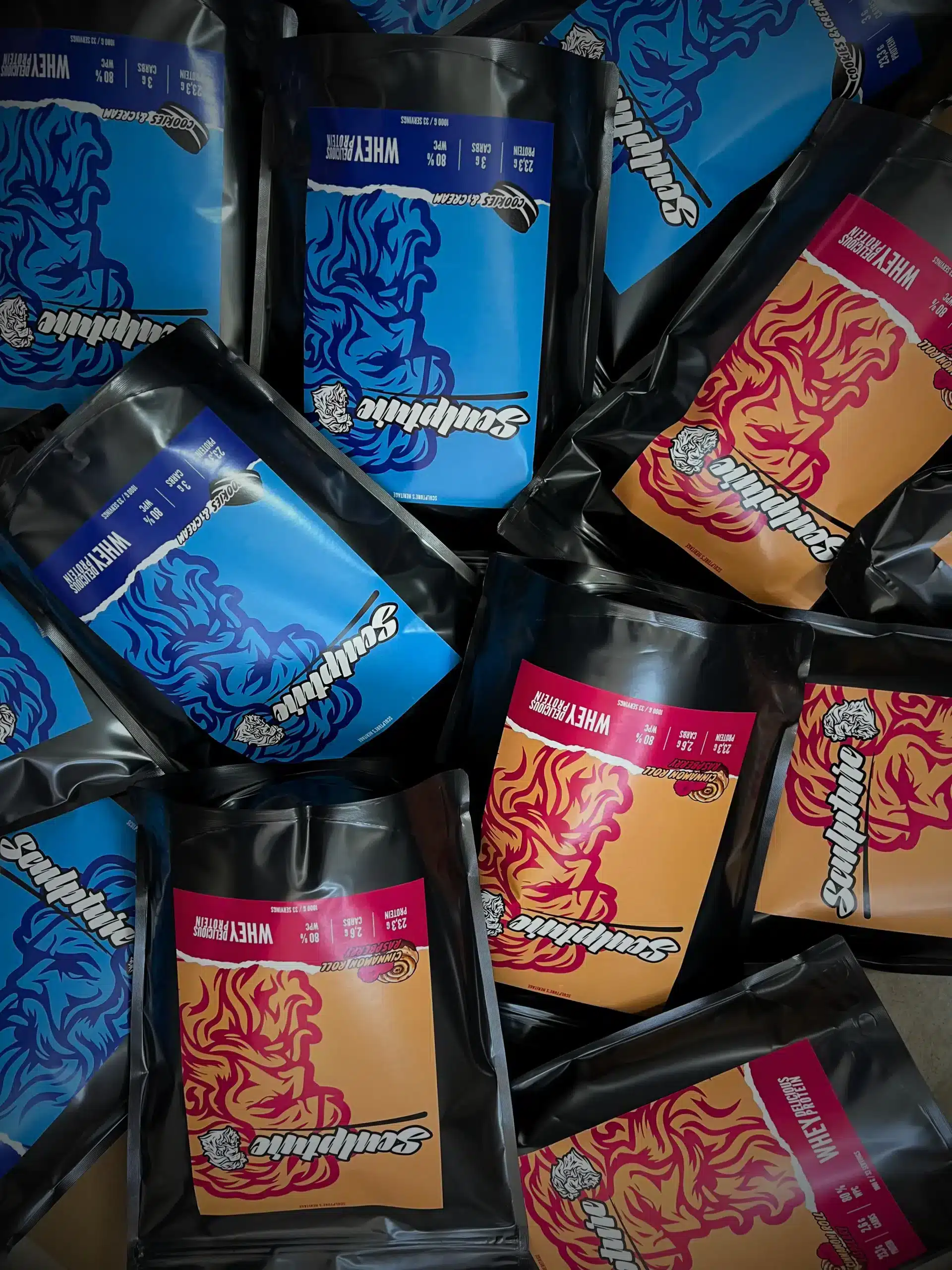 Sáčky whey proteinu Sculpture's Heritage v modrém a oranžovém provedení